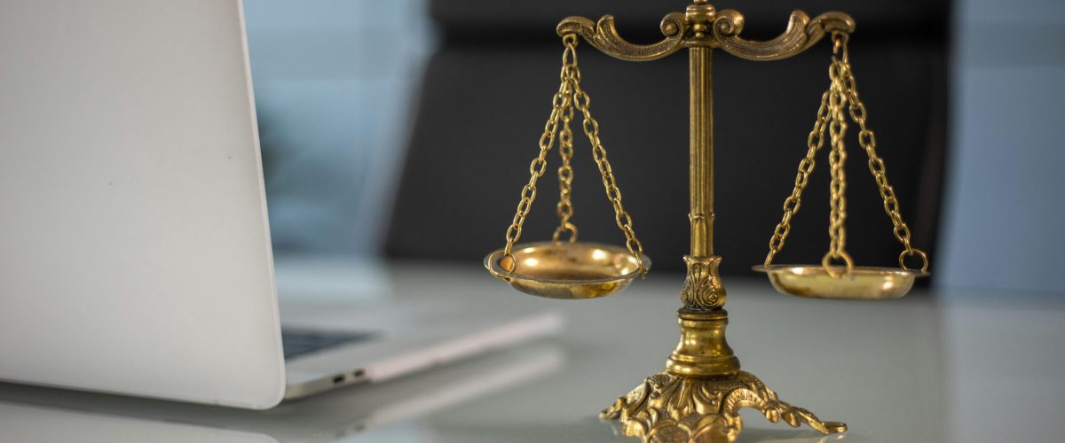 Golden justice scales on a desk beside a laptop, symbolizing law and balance.